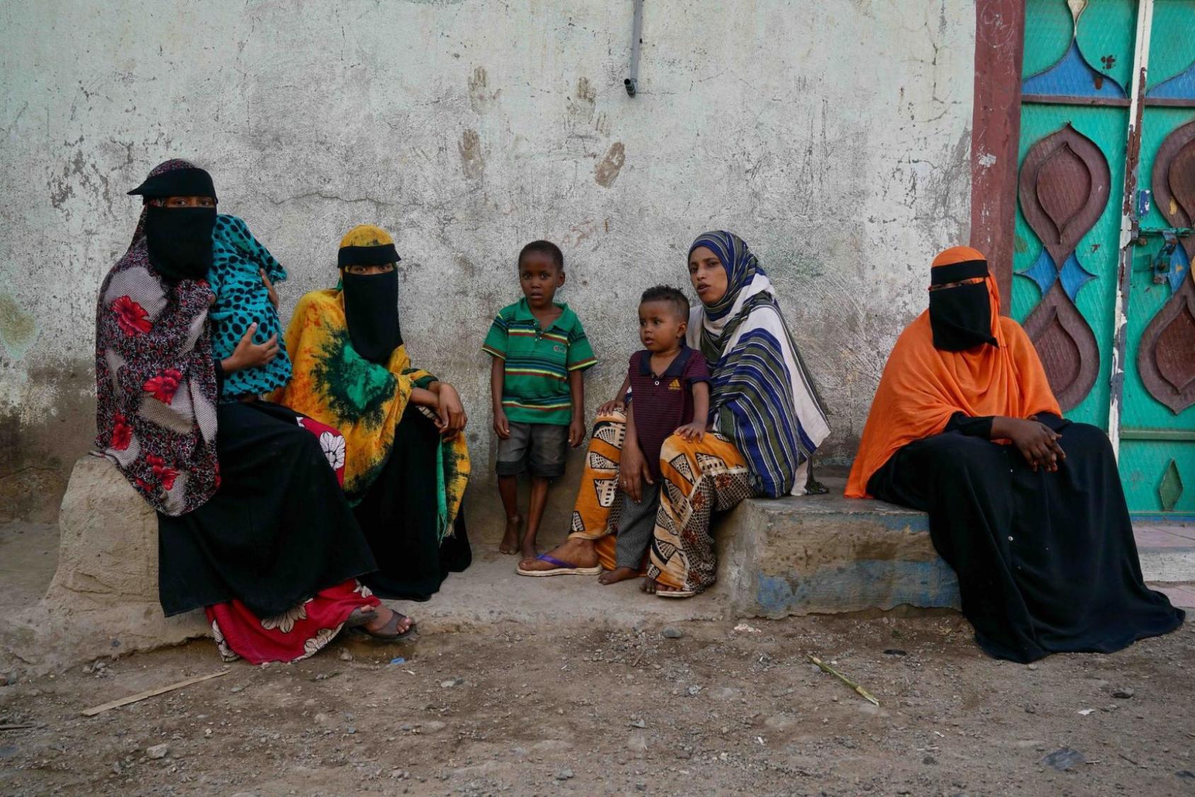 一群妇女和儿童坐在一条土路边上。