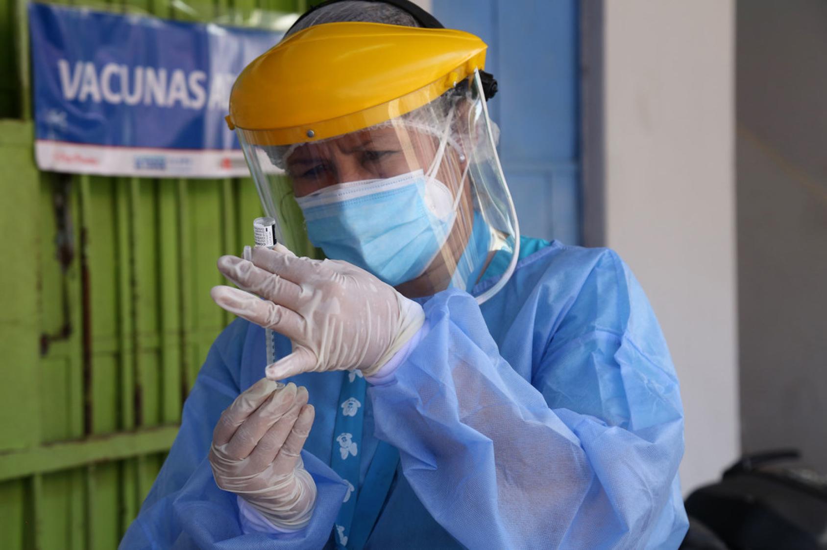Una trabajadora sanitaria, con equipo de protección individual, prepara una jeringuilla para administrar la vacuna contra el COVID-19.