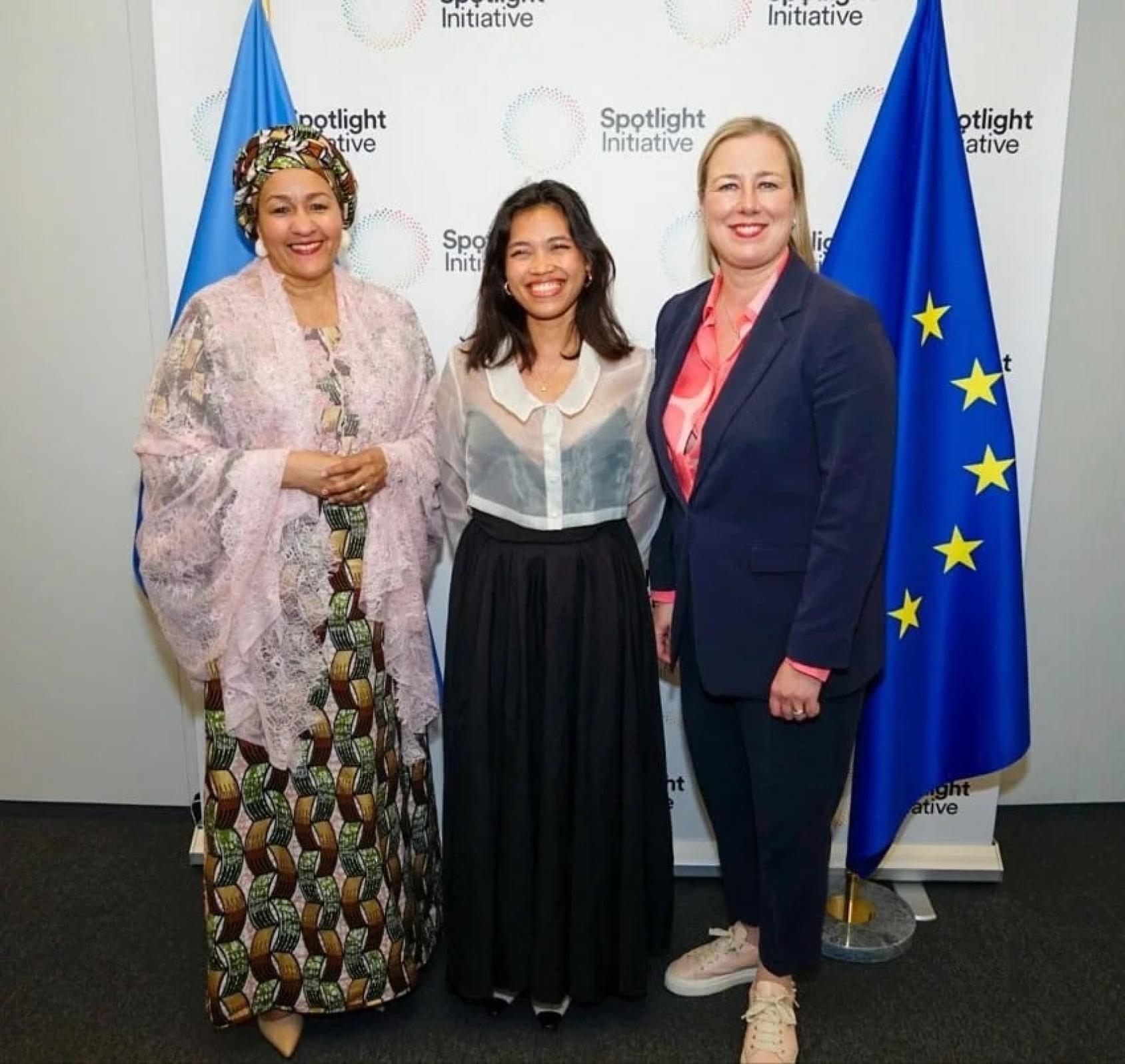 Three women stand in front of a white banner with the logo of the spotlight initiative printed on it. On either side of the banner you see the EU flag and the UN flag