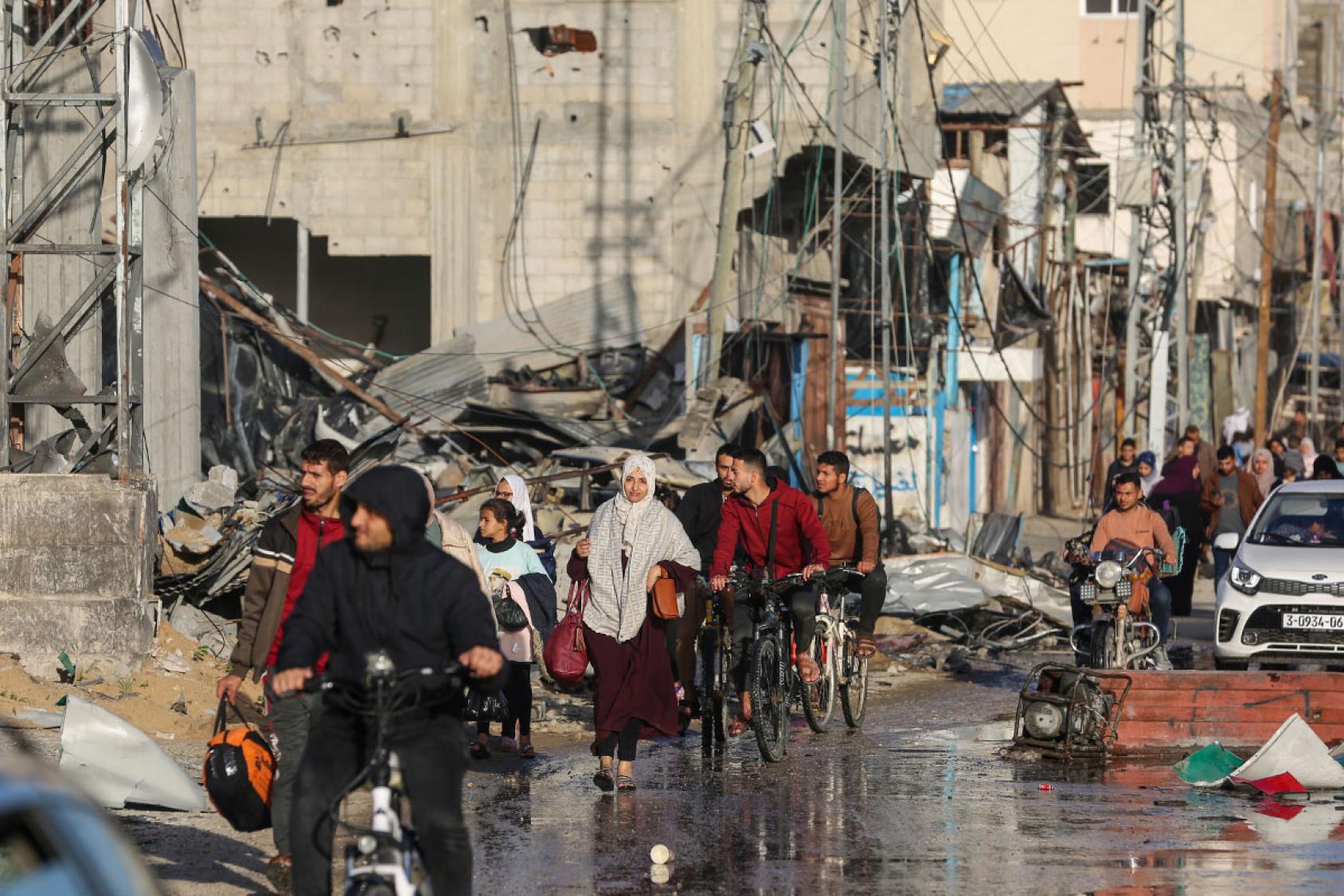 A group of people make their way through rubble and broken down buildings