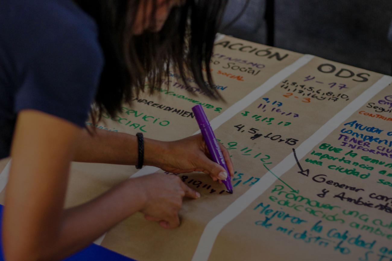 Une jeune fille écrit à l'aide d'un stylo-feutre sur une affiche posée sur une table.