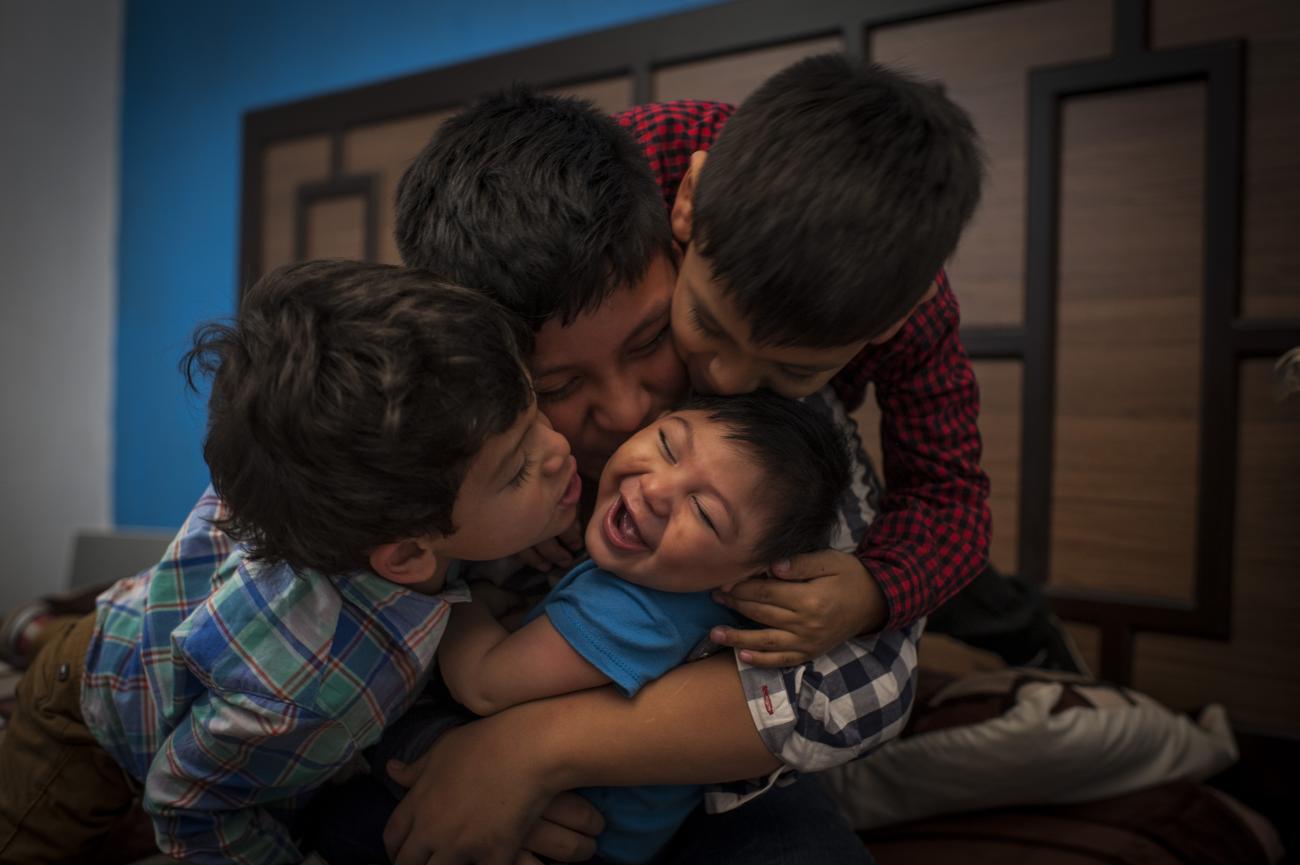 Image shows three brothers embracing and kissing their young baby brother. 