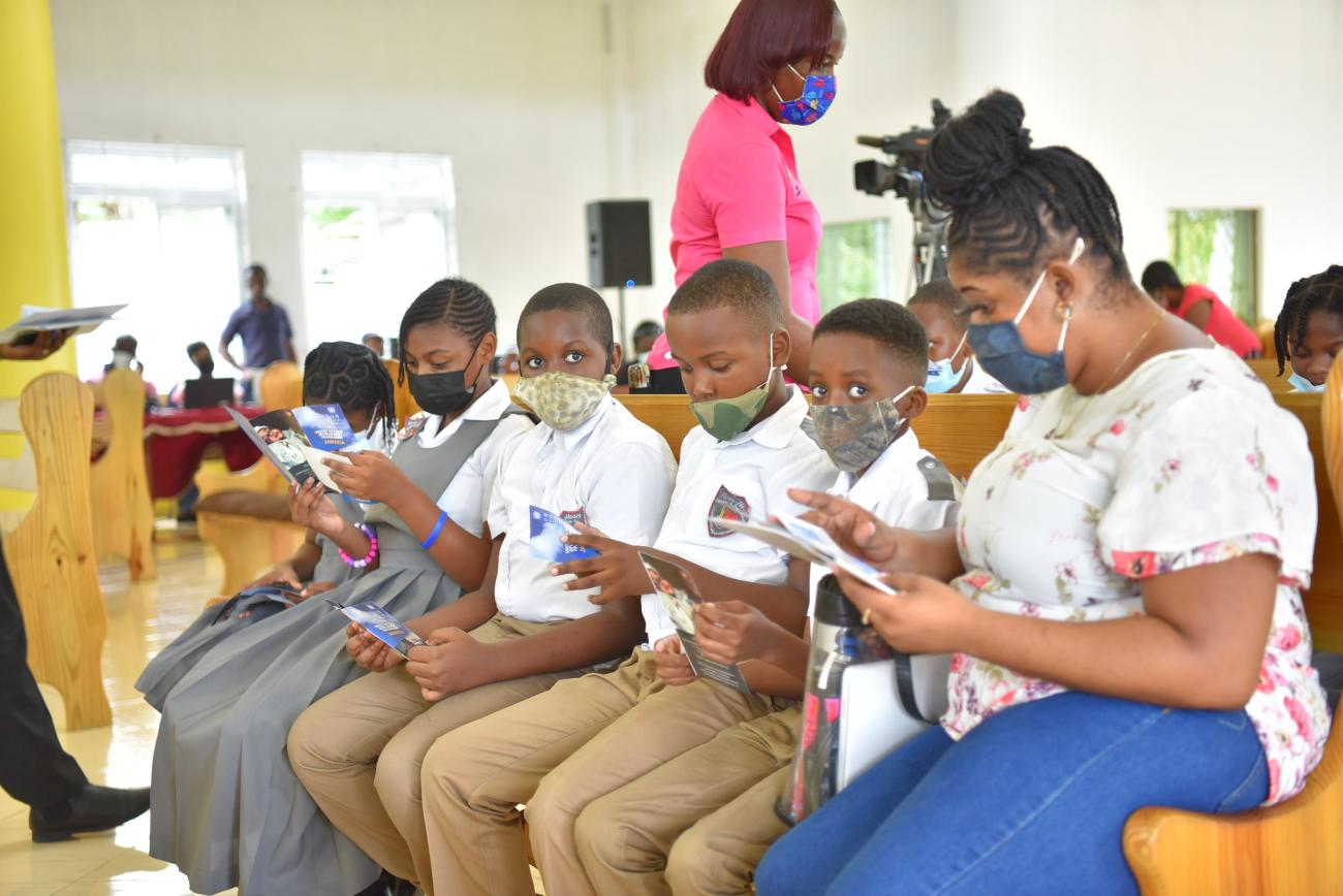 A row of schoolchildren in uniforms sit and read through books