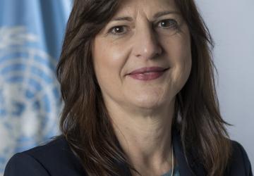 الصورة الرسمية لسوزانا سوتولي واقفة أمام علم الأمم المتحدة.