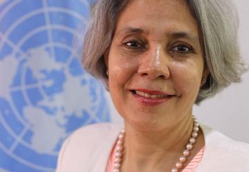 Official photo of Gita Sabharwal. She is shown smiling in front of the UN Flag. 