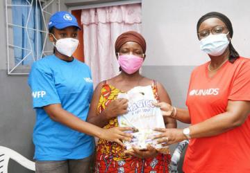 WFP and UNAIDS staff stand besides a woman holding a bag of essential supplies.