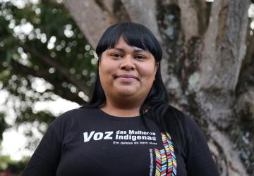 Una mujer indígena sonríe orgullosa con una franela negra con letras blancas, que dice "Voz de las mujeres indígenas".