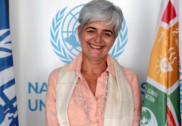 Portrait de Barbara Manzi, la nouvelle Coordonnatrice résidente des Nations Unies au Burkina Faso, souriant à la caméra devant le drapeau des Nations Unies et celui représentant les objectifs de développement durable.