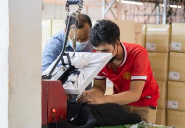 Deux personnes portant des masques de protection travaillent ensemble à la confection d'un vêtement dans une usine textile.
