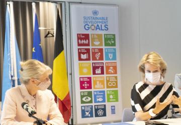 Director of the UN/UNDP Office in Brussels, and Her Majesty sit side-by-side at a desk in front of microphones. 