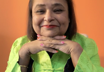 A woman in a bright green shirt holds her hands under her chin. 