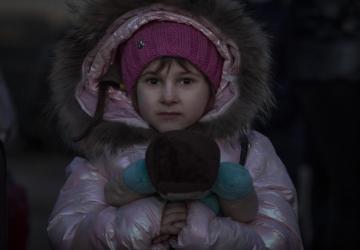 Una niña con un abrigo rosa acolchado sostiene un oso de peluche.