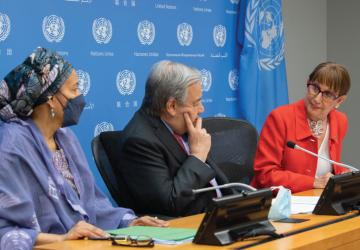 一名男子（联合国秘书长）坐在两名妇女之间，他们身后有联合国的标志。