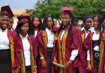 Varias mujeres jóvenes con trajes de graduación predominantemente morados se sitúan ante la cámara sonriendo con orgullo.