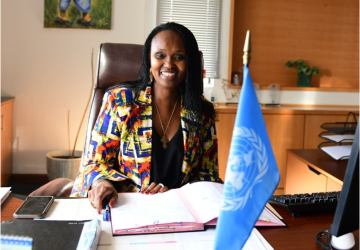 Femme dans une chemise colorée assise à un bureau avec un drapeau de l'ONU