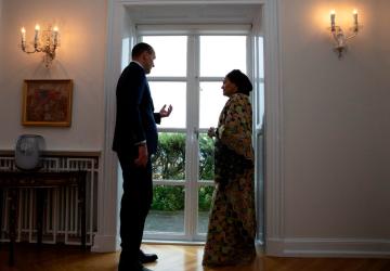 A UN official in a patterned dress stands next to an official in Iceland next to a window.