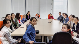 Des filles assises autour d'une grande table, dans une salle de réunion, se tournent vers l'objectif de la caméra.