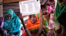Une jeune fille mauritanienne, entourée d'autres jeunes filles, toutes portant un voile coloré autour de la tête et des épaules, brandit un document au-dessus de sa tête en regardant l'objectif de la caméra.