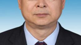 Head-to-shoulders close up of Sen Pang. He wears a dark suit, glasses and stands in front of a gradient blue background.