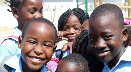 Close up of children from Beira, one of Mozambique’s largest cities, happily smile at the camera in front of a playground.