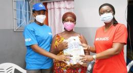 WFP and UNAIDS staff stand besides a woman holding a bag of essential supplies.