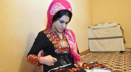 Lachyn, vêtue d’une tenue traditionnelle, est occupée à coudre un beau tissu coloré.