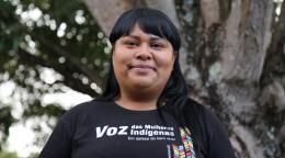 An indigenous woman smiles proudly wearing a t-shirt that reads Voice of the Indigenous women