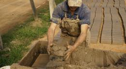Photo shows a brickmaker molding bricks by hand.
