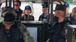 Gita Sabharwal, la Coordonnatrice résidente des Nations Unies en Thaïlande ((au centre) s’est jointe à une patrouille à bord d’une embarcation sur le Mékong. Elle porte une casquette bleue et indique du doigt un endroit au loin. Elle est entourée de plusieurs hommes vêtue de tenues militaires.