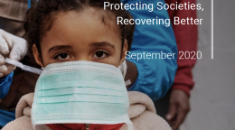 Cover shows a UN staff member helping to place a protective face mask on a young girl