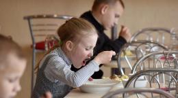 Tres pequeños en edad escolar (una niña y dos niños) comen, cada uno en su propia mesa.