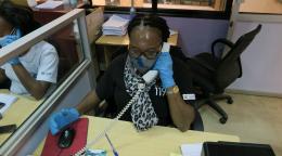 Une téléconseillère répond à un appel passé à la plateforme téléphonique du service d’aide aux victimes. Elle est assise à un bureau et porte un masque et des gants de protection.