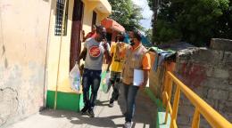 Des riverains et des membres du personnel de l’ONU longent les maisons d’un quartier de la République dominicaine. Ils portent un masque de protection et discutent entre eux en marchant.
