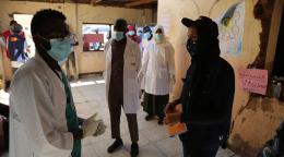 Les membres du personnel médical s’entretiennent avec le personnel de l'ONU dans le centre médical d’un camp. Les soignants portent tous des masques et maintiennent une distance de sécurité avec entre eux.