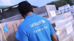 A man wearing a light blue UNICEF shirt looks over the delivery of vaccines wrapped in wrapping paper.