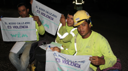 Trois hommes portant des tenues de travail jaunes regardent la caméra en tenant chacun entre les mains une serviette sur laquelle on peut lire, en espagnol : " El acoso calejero es violencia", ce qui signifie en français : "Le harcèlement de rue est une violence ".