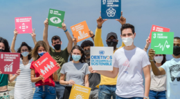 En la playa, un grupo de jóvenes, que usa mascarillas, sostiene carteles con los ODS.