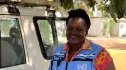 Женщина в светло-голубом жилете Организации Объединенных Наций улыбается в камеру. 