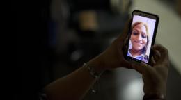 Una imagen de la mano de una persona sosteniendo un teléfono móvil, en el cual aparece la imagen de otra persona, en vio y directo.