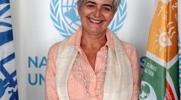 一名女性在联合国可持续发展目标旗帜和联合国标志前对镜头微笑。