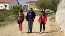 Three young girls walk down a dirt road in jackets. 