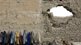 Varios abrigos colgados en percheros de pared, y a su derecha, hay un gran agujero en una superficie de ladrillos.
