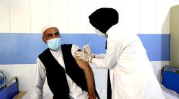 一位女性站着，为一名坐着的男性接种疫苗。