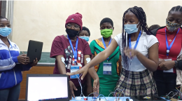 A group of young girls in masks point to computers. 