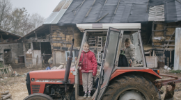 Two girls ride a run down tractor on a farm. 