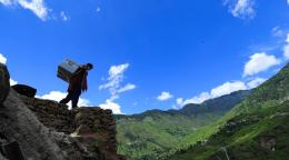 A silhouette of a woman with a large box on her back on top of a mountain on a beautiful day.