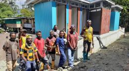 A group of men stand in front of multi-color latrines that they built. 