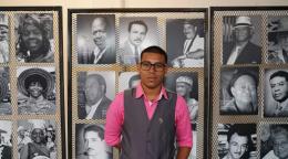 A young man stands in front of black and white portraits. 