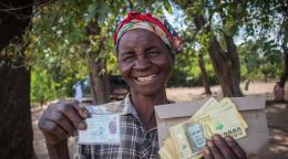 一位面带微笑的妇女举着现金援助和她的身份证。