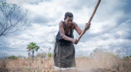 En Afrique, une femme travaille une terre aride à l’aide d’une pioche par un temps couvert.